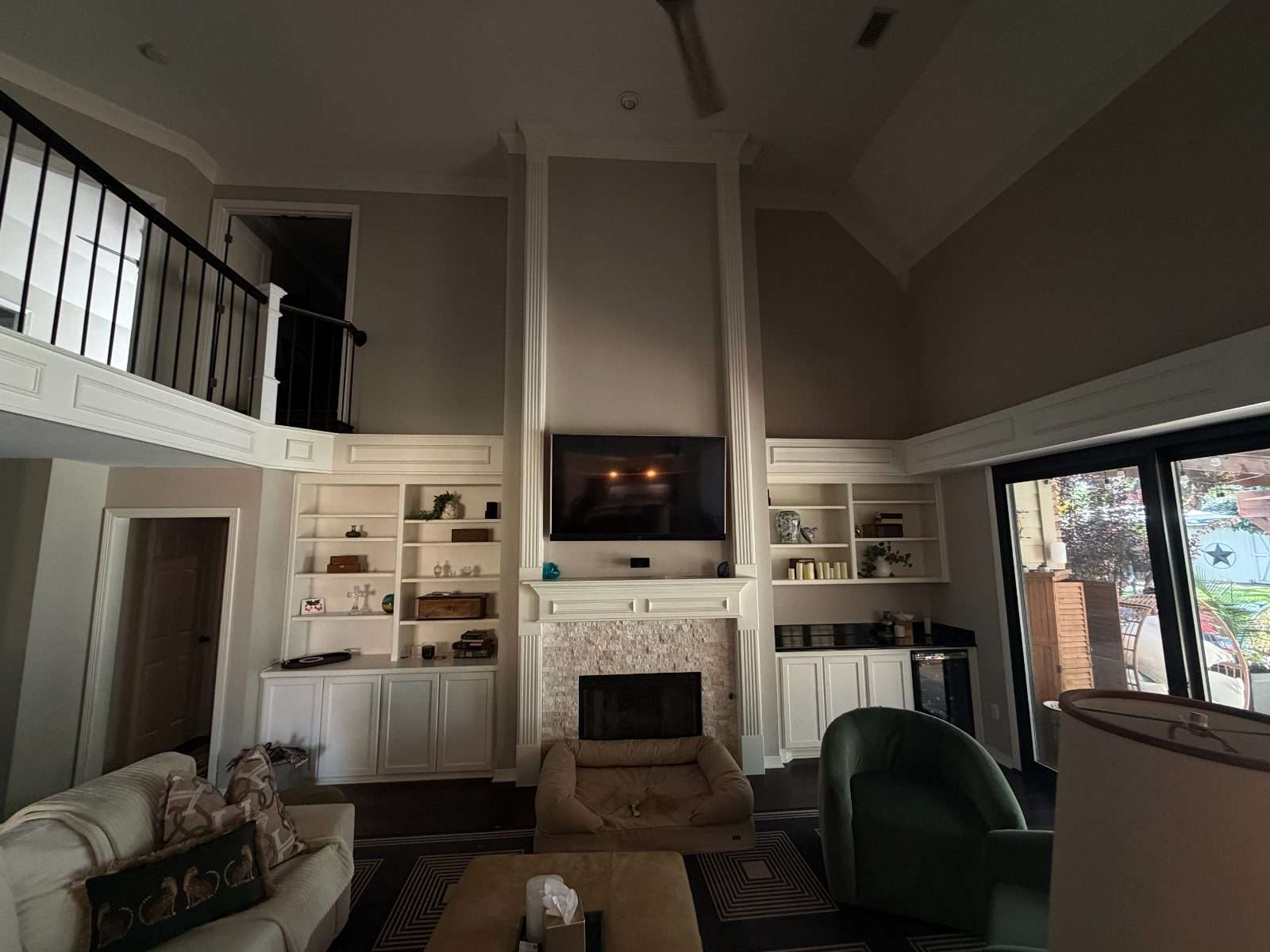 The living room in its existing condition before the remodel: a two-storey wall of white painted built-ins and fluted pilasters around a stacked-stone fireplace with a wall-mounted television