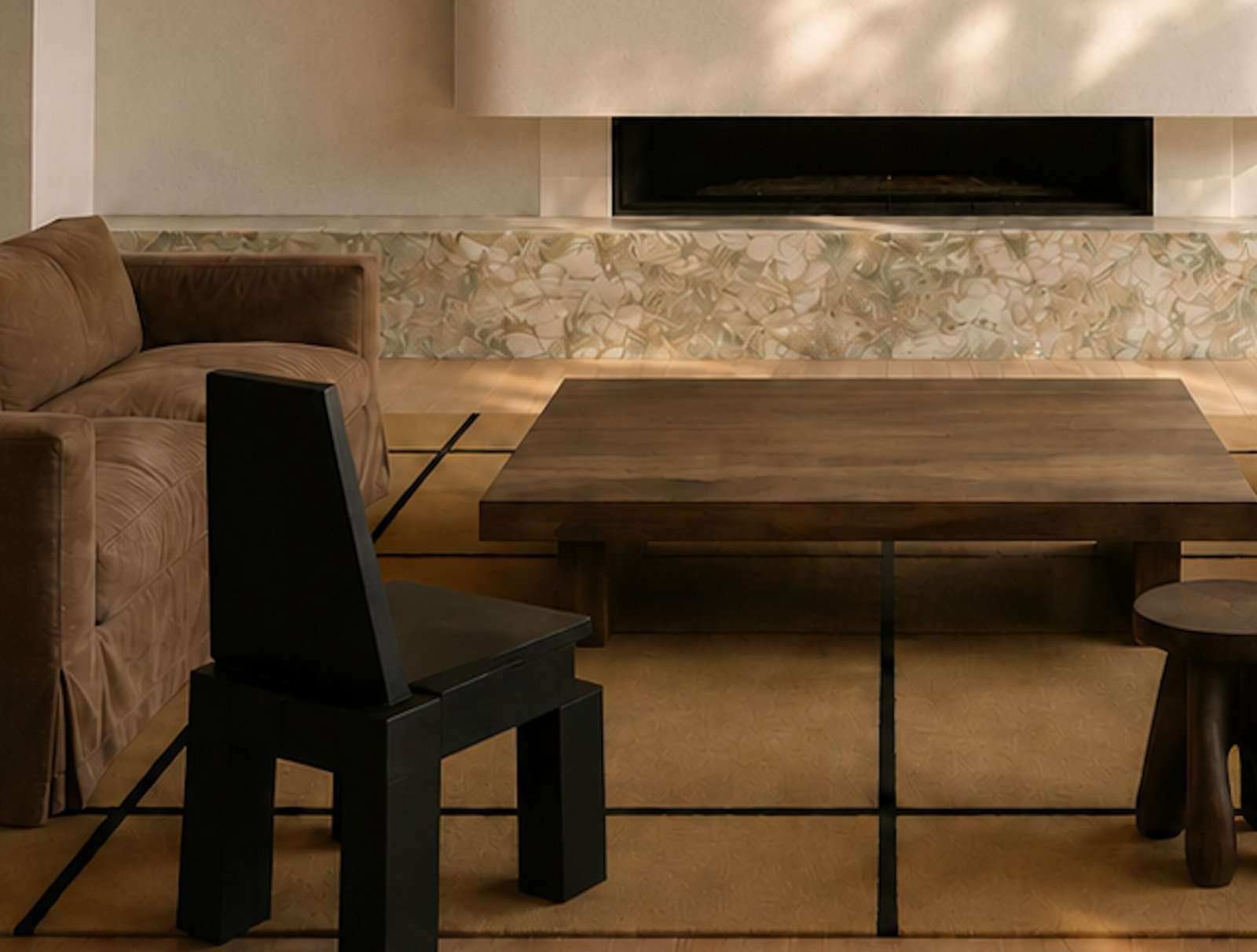 Artist impression — close view of the fireplace hearth: a long black firebox set into plaster in Shoji White by Sherwin-Williams, above a plinth of Fusion Wow by Antolini, with a heavy timber table, a brown velvet sofa and an angular black chair in front