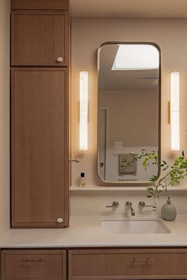 Vanity detail: a white oak storage tower beside a rounded mirror lit by two alabaster sconces, with a wall-mounted tap over an undermount basin