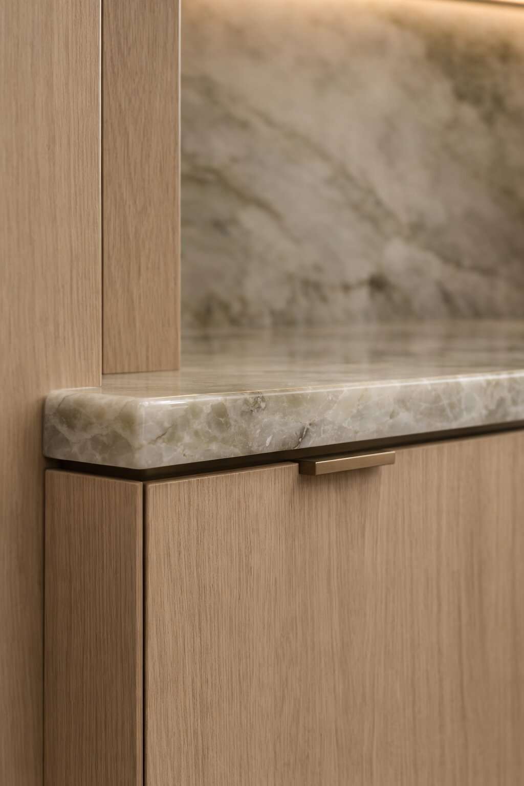 Artist impression — close detail of a pale oak cabinet meeting a thick pale stone shelf, with a slim bronze pull and a marble panel behind
